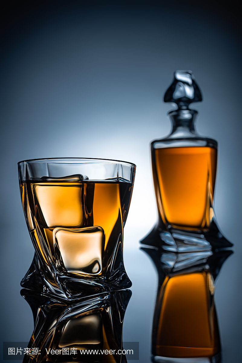 选择性地将威士忌酒杯与冰块和酒瓶的焦点放在灰色
